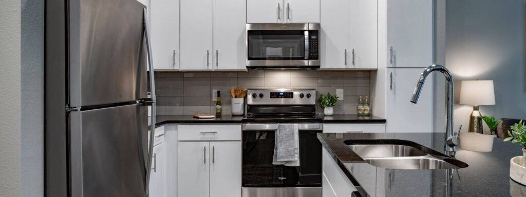 Modern kitchen with stainless steel appliances, white cabinets, a black countertop, and a sink with a chrome faucet. A striped towel hangs from the oven handle.