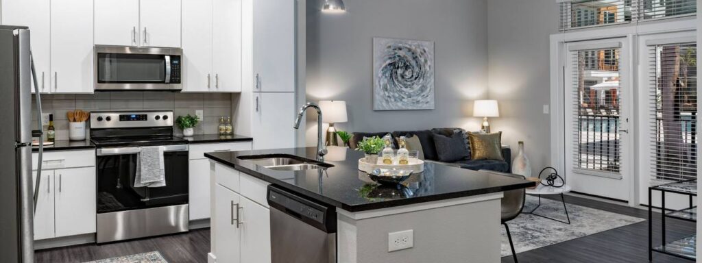 Modern kitchen and living area with white cabinets, black countertops, stainless steel appliances, and a cozy seating space. A painting and glass doors add a stylish touch.