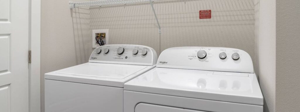 A laundry room with a white washer and dryer set under a wire shelf, with a photo frame and instructions above.