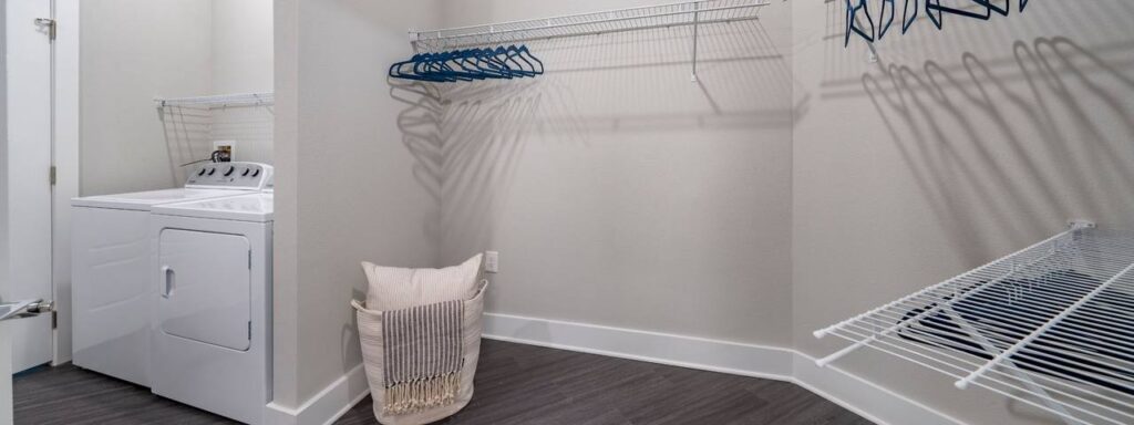 Laundry room with a washer and dryer, wire shelves, clothes hangers, and a laundry basket on the floor.