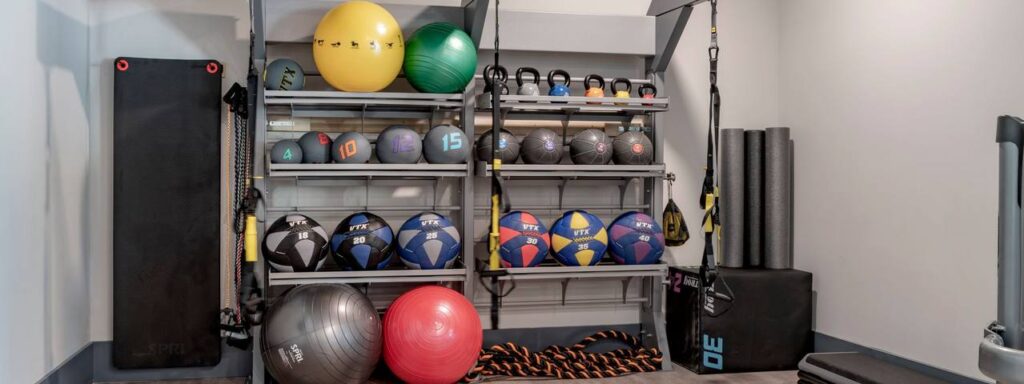 Home gym equipment organized on shelves, including medicine balls, kettlebells, exercise bands, foam rollers, and stability balls.