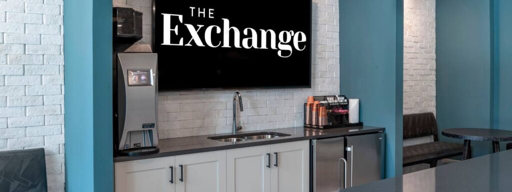 Coffee station with a beverage machine, sink, and cups. A large screen above displays "The Exchange.