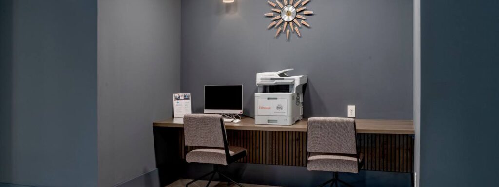 Office workspace with two chairs at a desk featuring a computer and a copier against a dark wall with a decorative starburst.