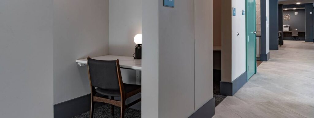 Quiet study area with a single desk and chair, and a small lamp on the desk, in a modern office space with neutral tones.