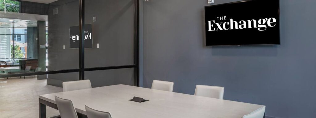 Modern conference room with a large table, chairs, glass wall, and a wall-mounted display reading "The Exchange.