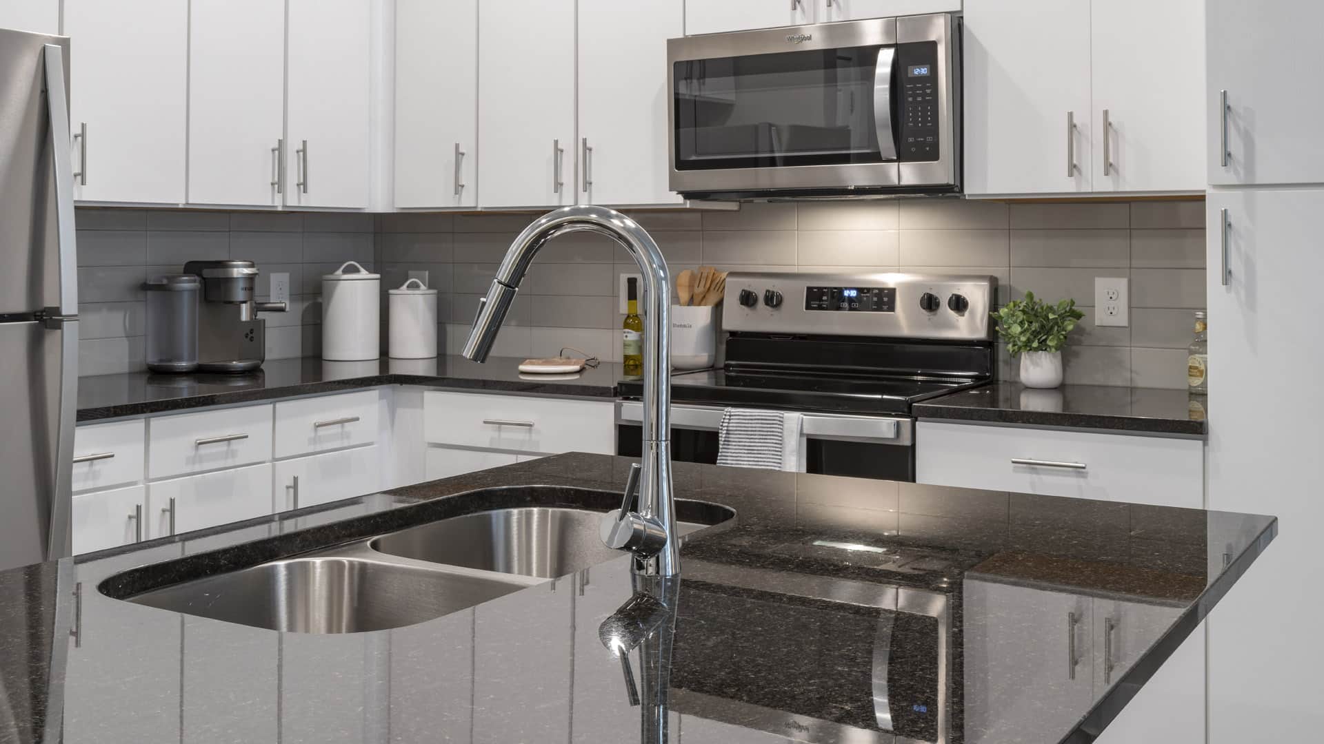 Modern kitchen with white cabinets, stainless steel appliances, black granite countertops, and a double sink with a chrome faucet.